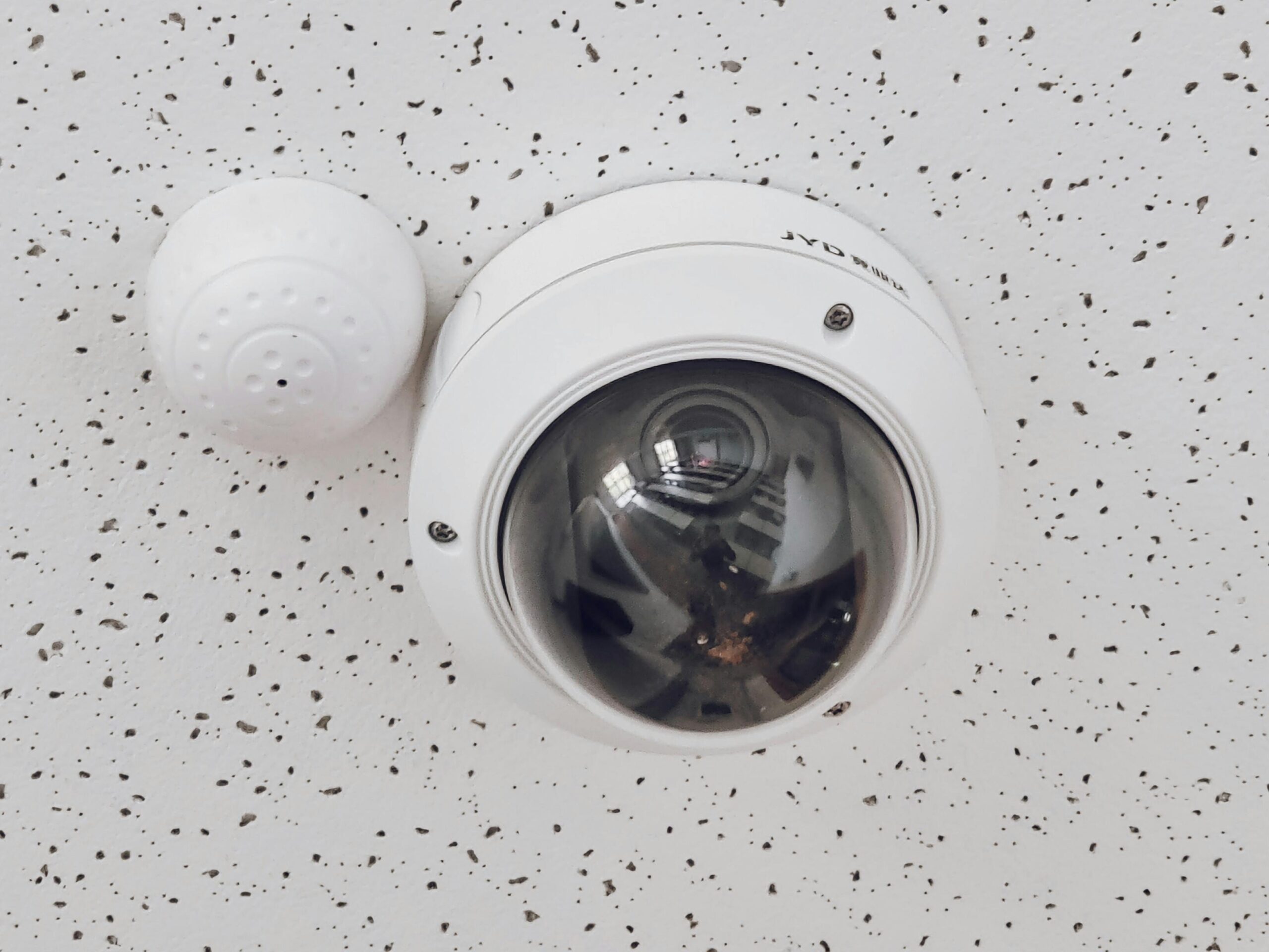 Close-up of a round dome surveillance camera installed on a speckled ceiling for security monitoring.